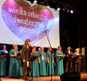 Chór na scenie. W tle logo Wielkiej Orkiestry Świątecznej Pomocy Chór na scenie. W tle logo Wielkiej Orkiestry Świątecznej Pomocy