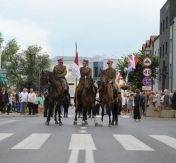 Odsłonięcie pomnika marsz. J. Piłsudskiego. Trzy osoby jadą na koniach środkiem ulicy. Za nimi spaceruje pochód mieszkańców.