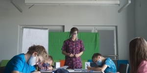 Czwórka dzieci siedząc przy stole pracuje nad zinami. Nad nimi czuwa osoba prowadząca warsztaty. Czwórka dzieci siedząc przy stole pracuje nad zinami. Nad nimi czuwa osoba prowadząca warsztaty.