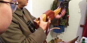 Na stole sprzęt wojskowy, człowiek prezentuje pistolet