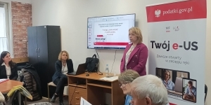 Jedna osoba stoi, kilka osób siedzi