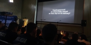ludzie siedzą, patrzą na napis na ekranie