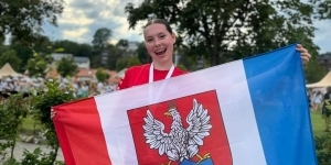 stoi jedna zawodniczka, trzyma flagę Legionowa stoi jedna zawodniczka, trzyma flagę Legionowa