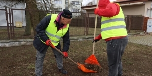 dwaj mężczyźni w odblaskowych kamizelkach grabią liście