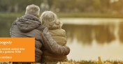 Zdjęcie przedstawia siedzącą parę seniorów nad brzegiem wody.