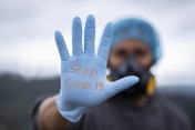 Mężczyzna z wyciągniętą dłonią. Na niej rękawiczka i napis: Stop Covid-19