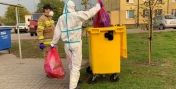 Na zdjęciu strażak w kombinezonie ochronnym wrzuca worki ze śmieciami do kontenera. Źródło: wirtualnelegionowo.pl