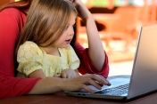 Na zdjęciu mama z dzieckiem - dziewczynką, siedzące przy laptopie.