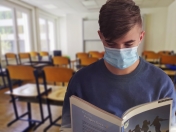 Na zdjęciu uczeń w maseczce czytający książkę na tle klasy.