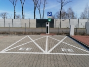 Na pierwszym planie znak - Parkuj i Jedź, w tle stacja do ładowania samochodów elektrycznych.