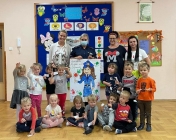 Na zdjęciu: mł. asp. Agata Halicka trzyma rysunek policjantki, wokół stoją dzieci z przedszkola i nauczycielki.