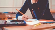 Osoba trzyma w ręku kredkę. Na pierwszym planie piórnik