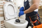 Osoba trzymająca przepychacz sanitarny nad muszlą klozetową