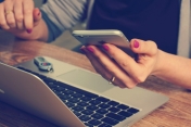 Osoba mająca ręce nad laptopem, w jeden z dłoni trzyma smartfon