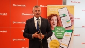 Mężczyzna przemawiający przez mikrofon, w tle reklama aplikacji do kupowania biletów Kolei Mazowieckich