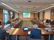 Sala konferencyjna, przy biurkach siedzą osoby i oglądają wyświetlane nagranie