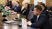 Mężczyzna siedząc mówi przez mikrofon, w tle kilka siedzących osób za stołami