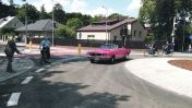 Kilka osób i różowe auto na rondzie