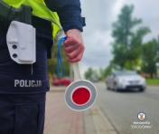 Stoi policjant przy jezdni, nadjeżdża samochód.
