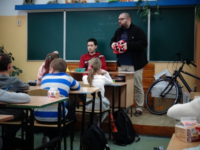 Zajęcia w klasie. Prowadzący pokazuje w jaki sposób prawidłowo zakładac kask.