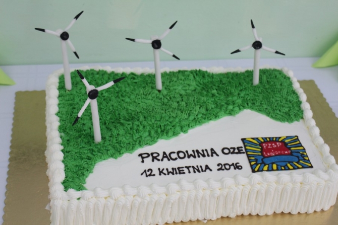 Kremowy Tort z napisem Pracownia OZE, 12 kwietnia 2016 obok logo PZSP Legionowo. Na torcie zamiast świeczek wiatraki.
