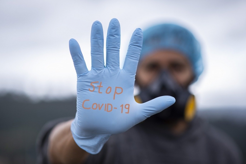 Mężczyzna z wyciągniętą dłonią. Na niej rękawiczka i napis: Stop Covid-19