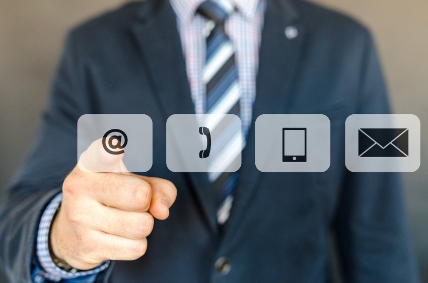 Cztery ikony kolejno od lewej małpa oznaczająca e-mail, telefon, tablet, wiadomość. Mężczyzna w tle wskazuje na ikonę e-maila. Źródło grafiki: pixabay.com