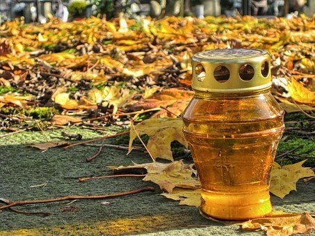 Na pierwszym planie znicz. W tle jesienne liście.