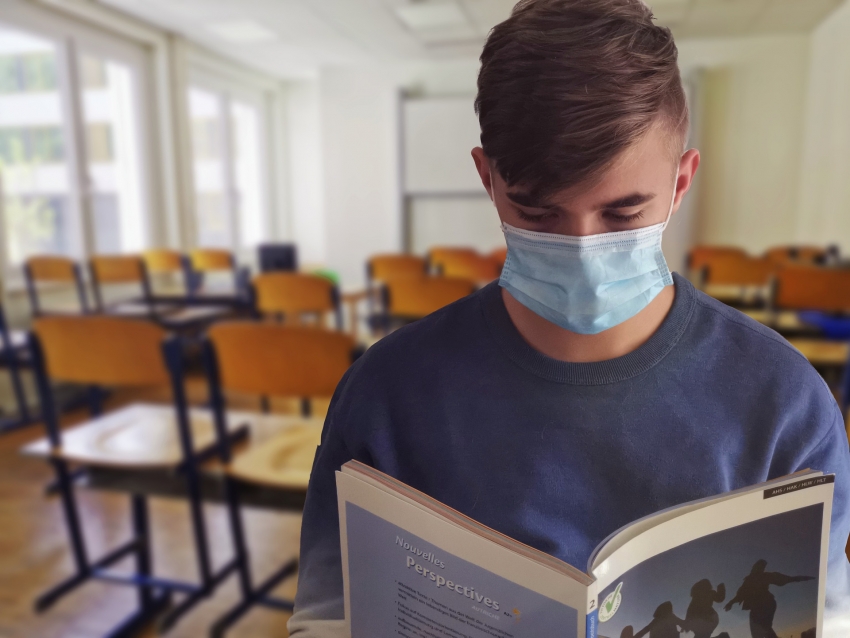 Na zdjęciu uczeń w maseczce czytający książkę na tle klasy.