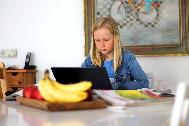 Na zdjęciu dziewczynka korzysta z laptopa. Na pierwszym planie znajdują się owoce oraz czasopisma.
