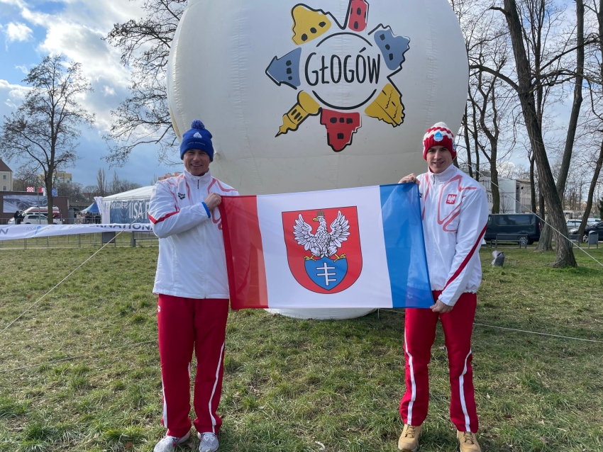 Dwóch mężczyzn trzyma flagę Legionowa, z tyłu logo Głogowa