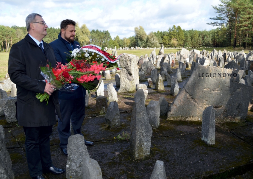 Dwóch mężczyzn trzymających kwiaty przy głazie z napisem Legionowo