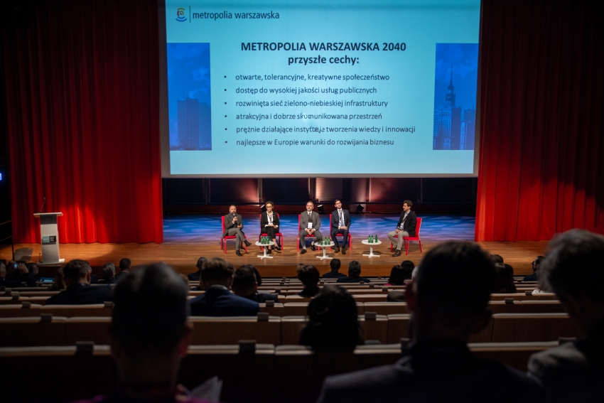 Pięć osób na scenie podczas konferencji, przed nimi widownia
