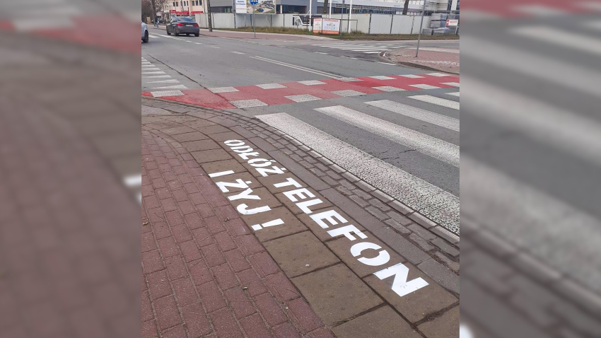 Ulica i chodnik, na jego skraju napis - Odłoż telefon i żyj