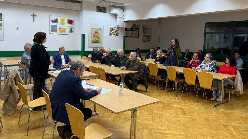 na sali przy stołach siedzą ludzie, dwie kobiety stoją