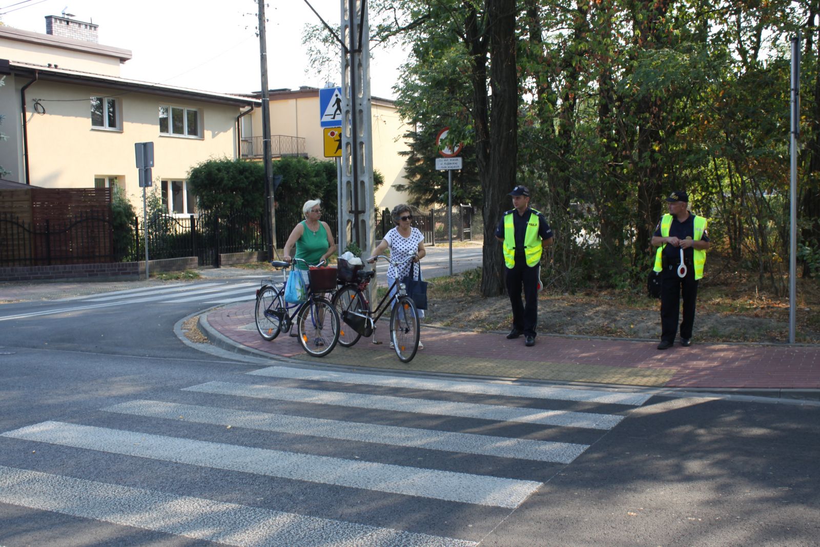 Dwóch rowerzystów i dwóch strażników miejskich przy przejściu dla pieszych